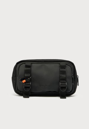 Svart nylonlomme med to glidelåslommer, vertikale stropper, en karabin-klips og preget logo. Jevn tekstur og kompakt rektangulært form.