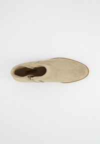 Bota de tobillo de ante beige con puntera puntiaguda, cremallera lateral y suela marrón. El interior presenta un estampado de logo, mostrando una textura suave.