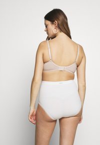 Sutiã bege com alças ajustáveis e fecho de gancho, emparelhado com cuecas brancas de cintura alta com renda ao longo das pernas.