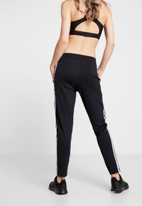 Black athletic joggers with white side stripes, elastic waistband, and tapered legs; paired with a black sports bra featuring a cutout back design.