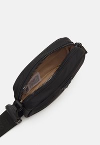 Sort nylon crossbody taske med lynlås, der har en beige indvendig med mesh-design. Inkluderer en justerbar rem og mærkehardware.