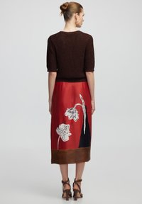 Top corto de punto marrón con mangas cortas, combinado con una falda de satén roja que presenta patrones florales en blanco y negro, y un dobladillo marrón.
