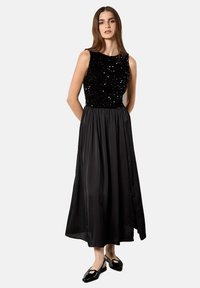 Schwarzes Abendkleid mit einem mit Pailletten besetzten Oberteil und einem fließenden Satinstoffrock. Die Silhouette ist ärmellos mit einer gerafften Taille.