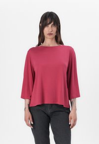 Bluză roșie, cu mânecă scurtă, cu un decolteu larg și o croială lejeră. Fabricată dintr-un material moale, ușor, cu o textură netedă.