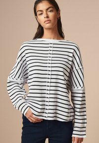 Maglione a righe bianche e blu navy con una vestibilità rilassata, dotato di un collo rotondo, spalle scese e sottili dettagli con bottoni lungo il davanti.