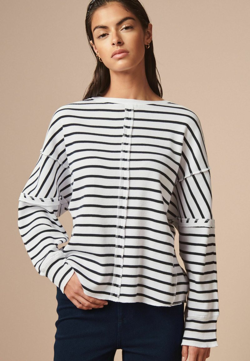 Maglione a righe bianche e blu navy con una vestibilità rilassata, dotato di un collo rotondo, spalle scese e sottili dettagli con bottoni lungo il davanti.