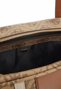 Sac à main brun à motif avec fermeture éclair, intérieur en tissu sombre et une petite étiquette de marque. Les accents incluent des poignées de couleur claire.