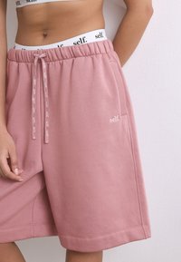 Shorts en coton rose avec une taille élastique, dotés d'un cordon de serrage et d'un petit logo. Texture lisse avec des poches latérales.