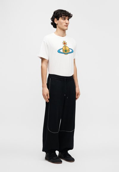 Λευκό μπλουζάκι με κίτρινο και μπλε γραφικό σχέδιο, συνδυασμένο με μαύρη φαρδιά φόρμα με αντιθετική ραφή και ελαστική μέση.