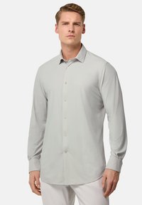 Camisa de manga larga gris claro con cuello abotonado, que presenta una textura suave y cinco botones en la parte delantera. Corte entallado con dobladillo redondeado.