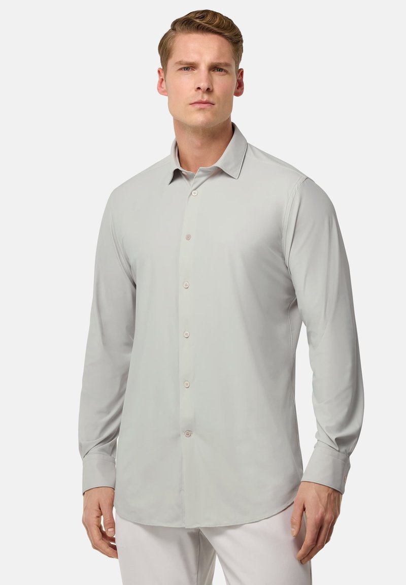 Camisa de manga larga gris claro con cuello abotonado, que presenta una textura suave y cinco botones en la parte delantera. Corte entallado con dobladillo redondeado.