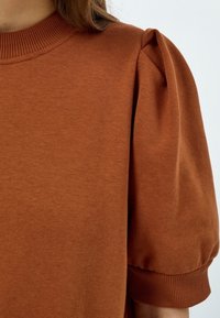 Orange-brown short-sleeve top featuring a ribbed neckline and puffed sleeves with elastic cuffs, made from a soft fabric.