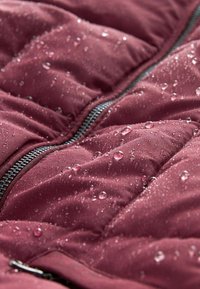 Tissu de doudoune bordeaux, texture matelassée avec des gouttes d'eau, contrastée par une fermeture éclair noire. La surface est lisse et légèrement brillante.