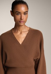 Pulover din tricot maro cu decolteu în V adânc, textură căptușită și mâneci largi, având o talie ajustată. Material moale și neted.