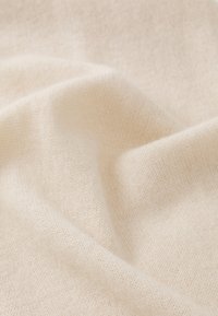 Tissu doux beige clair avec une texture tricotée fine, présentant de douces ondulations et de subtiles variations de couleur et d'épaisseur.