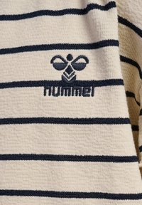 Krèmfarvet stof med navy horisontale striber, med tekstureret overflade, prydet med et Hummel-logo broderet i navy.