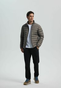 Puffjakke i dæmpet grå med vandret quilting, lynlås og høj krave. Sørget med sorte cargo-bukser og brune vandresko.