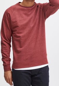 Rood gemêleerd sweatshirt met lange mouwen, geribbelde boorden en zoom. Bevat een ronde halslijn en een textuurstof. Steekdetails bij de naden.