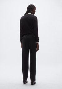 Zwarte trui met een ronde hals en lange mouwen, gecombineerd met zwarte broek met een losse pasvorm en elastische tailleband.