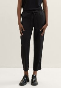 Schwarze, leichte Hosen mit elastischem Bund, schmal zulaufenden Beinen und glatter Textur; kombiniert mit schwarzen Schnürschuhen.
