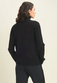 Pull à col roulé noir avec des détails côtelés aux poignets et à l'ourlet. Texture douce, coupe décontractée et design minimaliste. Vue arrière présentée.
