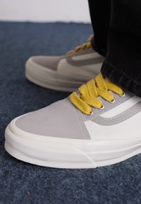 Gray and white sneakers with a smooth leather upper, yellow laces, and rubber soles. Features stitching and side accents.