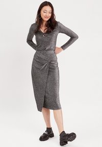 Abito midi grigio lucido con maniche lunghe, scollatura curvata, dettaglio torcigliato in vita, orlo obliquo, abbinato a scarpe chunky nere.