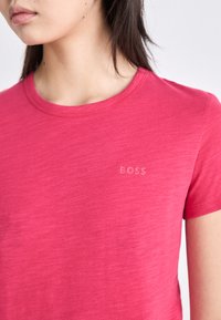 Rozā īsām piedurknēm T-krekls, kas izgatavots no viegla auduma, ar apaļu dekoltē un smalku "BOSS" logo gaišākā tonī uz krūšu daļas.