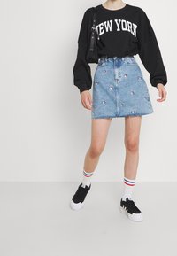 Czarny sweter z nadrukiem "NEW YORK", jasnoniebieska spódnica dżinsowa z haftem kwiatowym, czarne sneakersy i białe skarpetki w kolorowe paski.