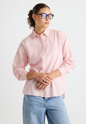 Chemise boutonnée rose pâle en tissu doux avec manches longues, dotée d'un col classique et d'une coupe décontractée, associée à un jean bleu.