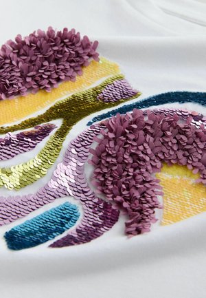 Witte stof met een kleurrijk ontwerp met paarse, gele, groene en blauwe pailletten en gestructureerde stoffen bloemblaadjes in verschillende vormen en maten.