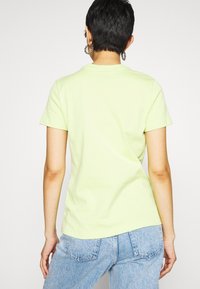 Ljusgrön kortärmad t-shirt med rund halsringning, gjord av mjukt bomull, med avslappnad passform och rena sömmar, bärs tillsammans med ljusblå jeans.