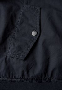Marinblå jacka med detalj av en vänster bröstficka med en svart tryckknapp märkt "Cecil" och elastisk nederkant för en figursydd passform.