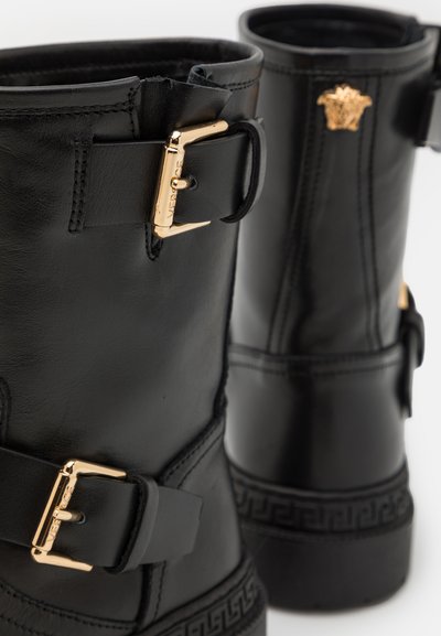Bottines en cuir noir dotées de quincaillerie dorée, d'accents de boucle et d'une semelle en caoutchouc à motifs. Le design comprend un emblème de marque.
