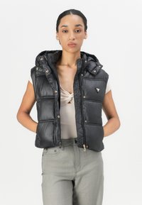 Zwarte gepolsterde vest met capuchon, met een glanzende textuur, gouden hardware en een ritssluiting aan de voorkant. Het vest heeft twee zijzakken en een merklogo.