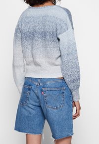 Pull gris clair aux nuances dégradées de bleu, tricot texturé, ourlet côtelé. Associé à un short en jean bleu avec une poche classique Levi's.