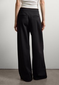 Pantalones de pierna ancha negros con una textura suave, que cuentan con una cintura alta y dos discretos bolsillos traseros.