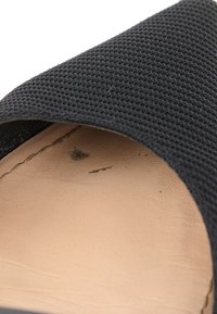 Gros plan de la semelle intérieure d'une chaussure avec une doublure beige et une bride en tissu noir texturé sur le bord supérieur.