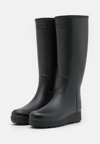 Bottes de pluie noires en caoutchouc, montant jusqu'aux genoux, avec un bout arrondi, une semelle texturée et des accents de logo en relief sur les côtés. Fini lisse, design imperméable.