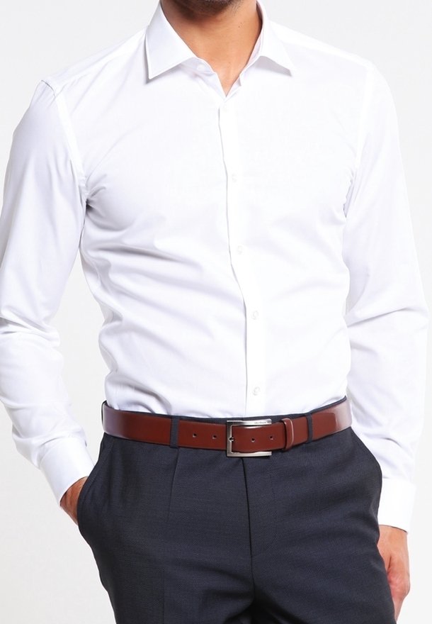 Witte blouse met lange mouwen en knopen, slim fit, gecombineerd met donkergrijze broek en een bruine leren riem met een zilveren gesp.