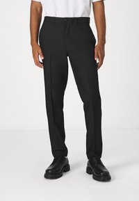 Pantalones de vestir negros hechos de una tela ligera, con un corte recto, dos bolsillos laterales y un acabado suave. Combinados con zapatos de vestir negros.
