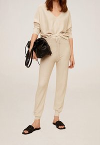 Ensemble d'intérieur en maille beige comprenant un haut à col en V et un pantalon à cordon de serrage. Sac en cuir noir et sandales à enfiler au design texturé.