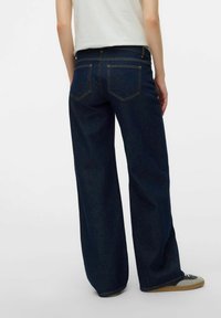 Dark blue wide-leg jeans made of denim, featuring back pockets and a high waist, paired with gray sneakers on a light background.