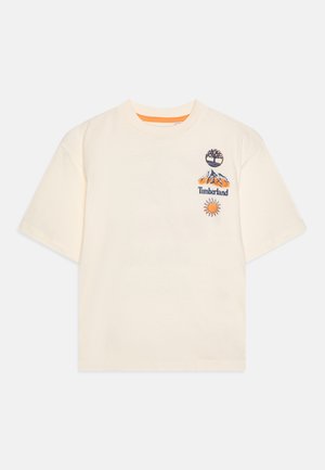 T-shirt crème à manches courtes avec des logos brodés en motifs : un arbre, des montagnes avec "Timberland", et un soleil. Col rond. Matière en coton doux.