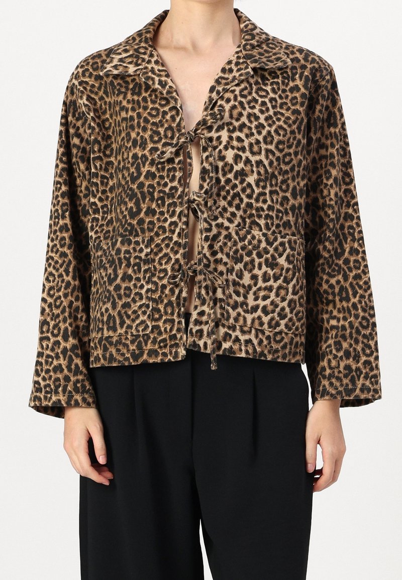 Veste à imprimé léopard avec trois liens à l'avant et grandes poches plaquées portée sur un pantalon noir par un mannequin.