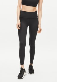 Svarta träningstights med hög midja, stretchigt material, slät textur, åtsittande design, ihop med svarta sneakers.