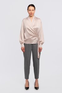Seidenbluse in sanftem Beige mit langen Ärmeln, kombiniert mit maßgeschneiderten grauen Hosen und schwarzen High Heels. Glatte Textur und elegantes Design.