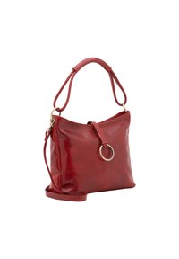 Sac à main en cuir rouge au design épuré, avec une poignée arrondie, une bandoulière amovible et un accent circulaire proéminent.