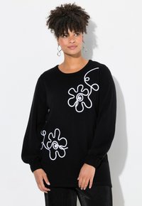 Schwarzer Pullover aus weichem Strickmaterial mit weißen floralen Mustern auf der Vorderseite und langen Ärmeln mit gerippten Bündchen.