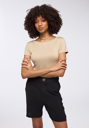 Top beige a maniche corte realizzato in tessuto morbido, abbinato a pantaloni corti neri su misura con chiusura frontale a bottone e design testurizzato.